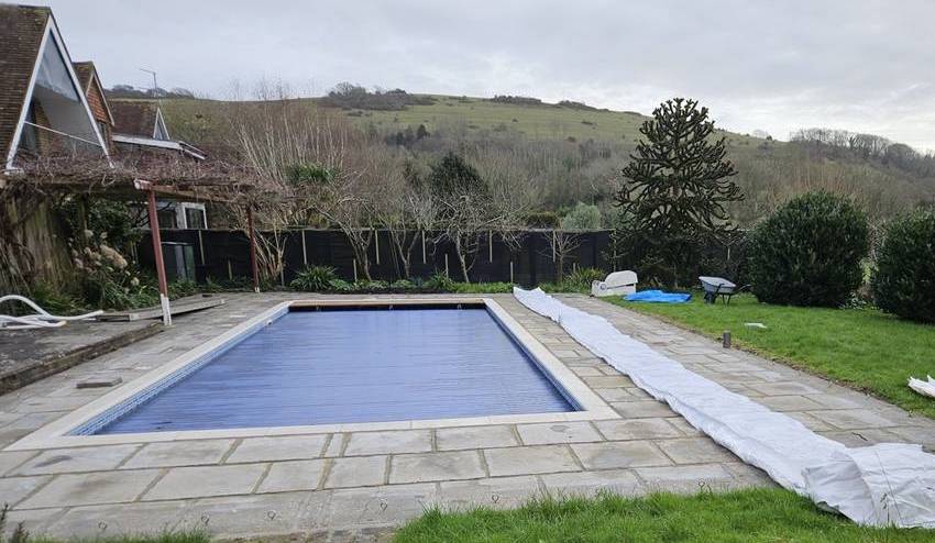 Installation preparation for an inflatable pool dome, with the cover laid out flat on a patio next to a swimming pool in a UK backyard.