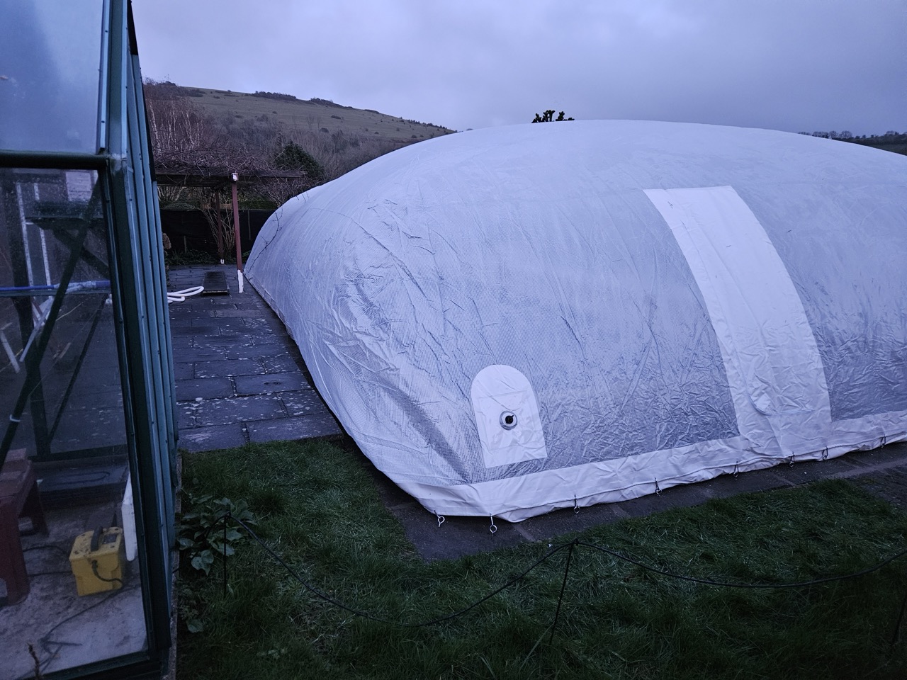Close-up of the entry point on an inflatable pool dome, showing the reinforced access door and secure attachment to the patio in a UK garden.