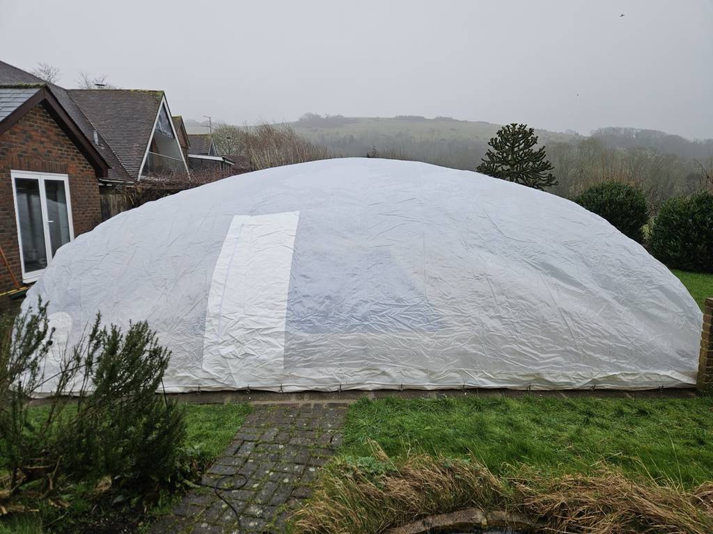 Inflation process of a transparent pool dome, showing the structure taking shape over a residential swimming pool in a garden.