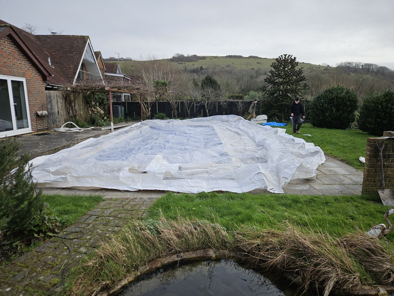 Installation process of an inflatable pool dome in a UK garden, showing the dome being laid out and prepared for inflation over a swimming pool.