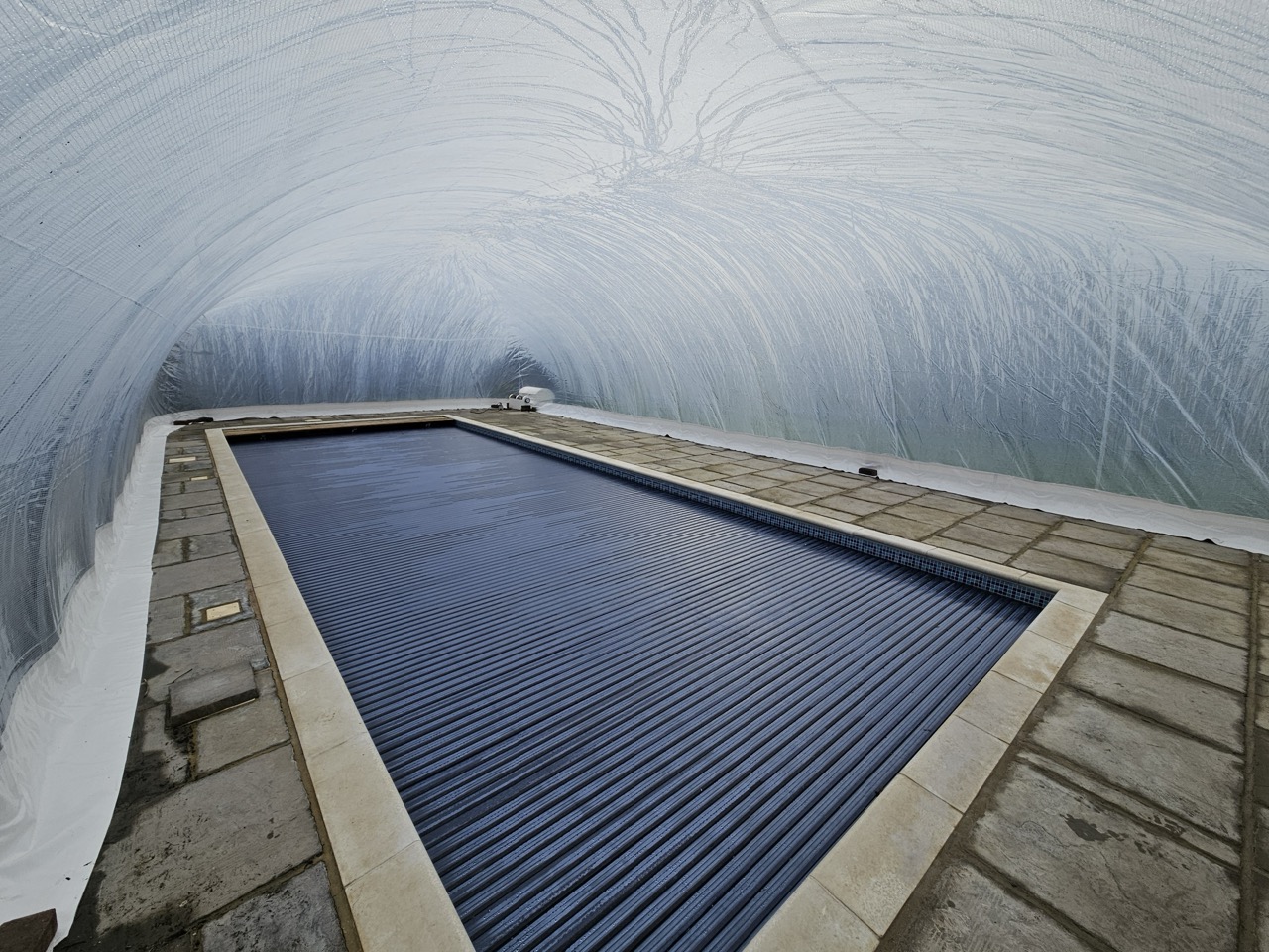 Inflatable pool dome covering a swimming pool with an automatic retractable cover, demonstrating dual protection and energy efficiency for UK homeowners.